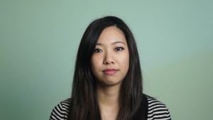 Person wearing a striped shirt looking thoughtfully into the camera, against a sage background