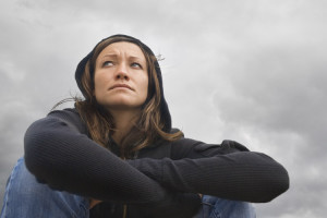 A feminine-presenting person hugging her knees with a pensive expression.