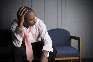 A person sitting in a waiting room has their hand on their head and their tie loosened in frustration and exhaustion