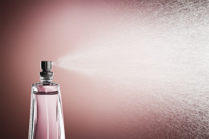 Glass bottle of pink perfume spraying a fine mist against a pink background