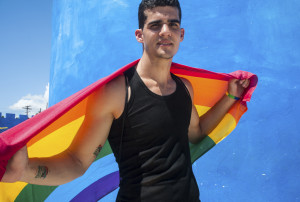 A person stands confidently staring into the camera with a rainbow flag draped over their shoulders.