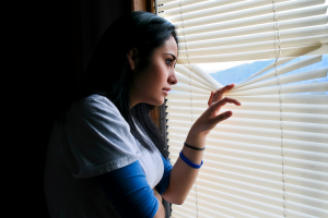 Person looking nervously out the window, trying not to be seen