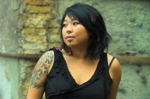 Tattooed person standing against a brick wall, looking into the distance