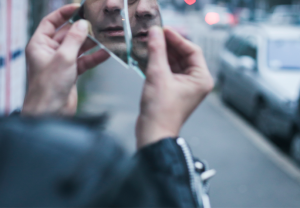 A person holds up broken glass to look at their reflection